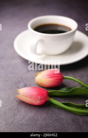 tulipano rosa e tazza di caffè su sfondo nero Foto Stock