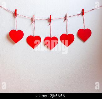 Carta rossa a cuore tagliata con cordoncino naturale e clip rosse appese alla parete, spazio copia, giorno valentine - immagine Foto Stock