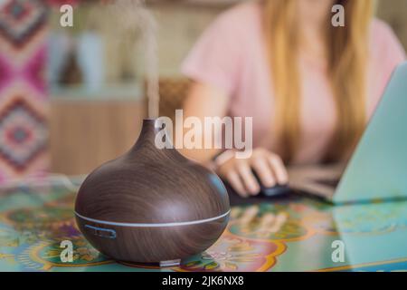 Diffusore di olio essenziale sul tavolo che fuma mentre la donna usa un computer portatile Foto Stock