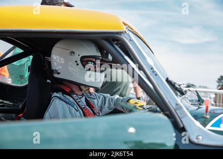 Un pilota di auto da corsa seduto nella sua auto indossando un casco e occhiali da sole Foto Stock