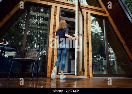 Vista posteriore di una donna che entra nella cabina forestale Foto Stock