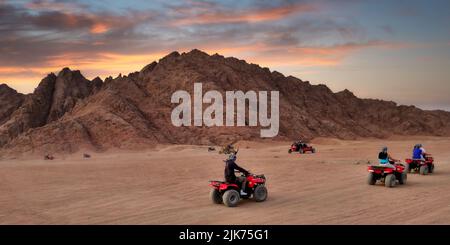 Un uomo irriconoscibile in quad rosso nel deserto egiziano di Sharm el-Sheikh al tramonto Foto Stock
