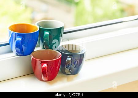 Quattro tazze multicolore in ceramica sul davanzale. Tempo di rilassamento di te' e caffe' Foto Stock