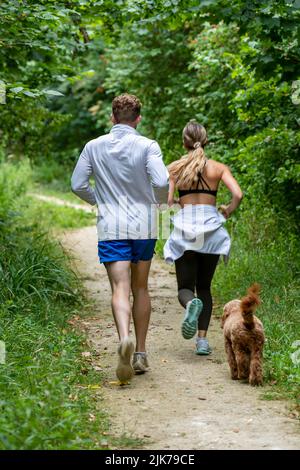 giovane coppia uomo e donna che corrono nel bosco con il loro cane, mantenersi in forma insieme, coppia che corrono nel bosco, coppia che corrono con il cane, cane a piedi. Foto Stock