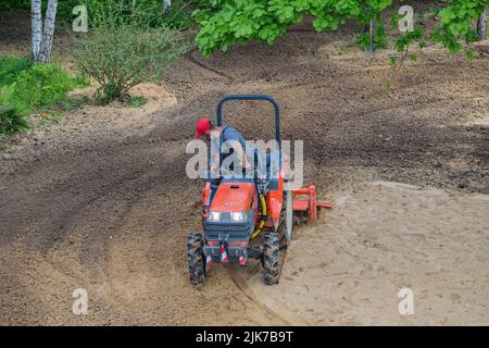 Un agricoltore su un mini trattore allenta il terreno per il prato. Coltivazione di terra, livellamento di superficie. Foto Stock