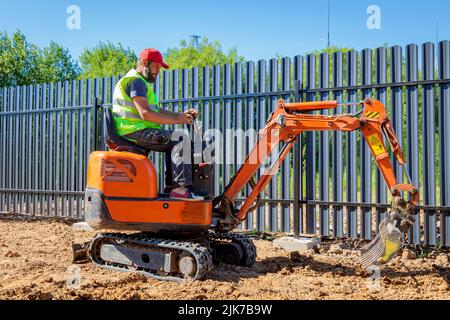Un uomo su un miniescavatore livella un pezzo di terra, allenta il terreno Foto Stock