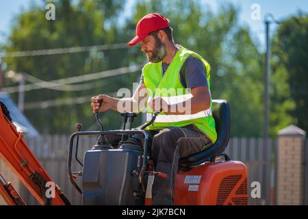 Un uomo su un miniescavatore livella un pezzo di terra, allenta il terreno Foto Stock