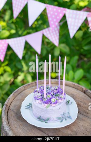 Bellissima torta bento con viola, veri peri, fiori di mattiola con foglie verdi, candele nella torta sullo sfondo di bandiere rosa. Compleanno. Foto Stock