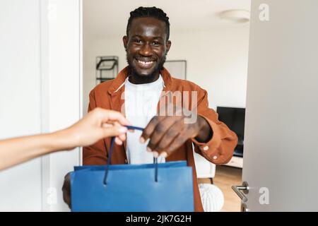Servizio di consegna acquisti. Felice uomo afroamericano ottenere borse shopper dal corriere e sorridendo alla macchina fotografica Foto Stock