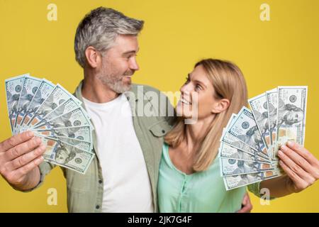 Grande fortuna e vincere concetto. Sposi maturi felici che tengono i contanti molto del dollaro, posando con i soldi sopra lo sfondo giallo Foto Stock