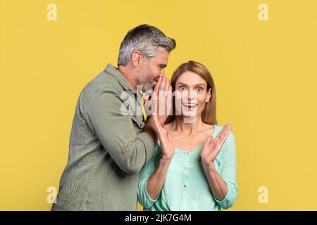 Uomo di mezza età che condivide segreto o sussurrando i pettegolenti nell'orecchio di sua moglie, coniugi che condividono notizie scioccanti Foto Stock