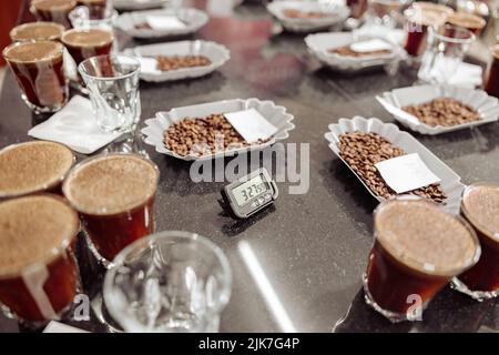 Bicchieri di caffè e ciotole con caffè torrefatto in chicchi pronti per una degustazione di caffè Foto Stock