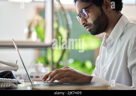 Un uomo d'affari indiano occupato programmatore che lavora a scrivere su un computer portatile seduto alla scrivania. Foto Stock