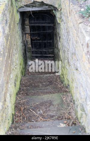 Antichi gradini in pietra che conducono a una porta di legno intemprata in uno storico passaggio sotterraneo Foto Stock