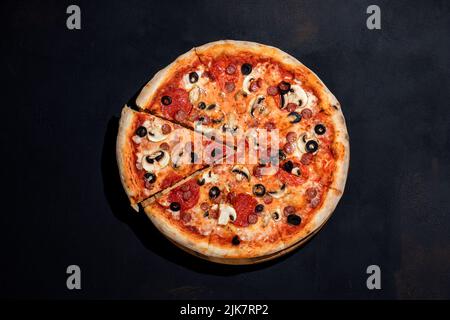 Pizza a base di pomodoro con mozzarella, salsicce da caccia, salame, olive, salsa di funghi su sfondo nero. Foto Stock