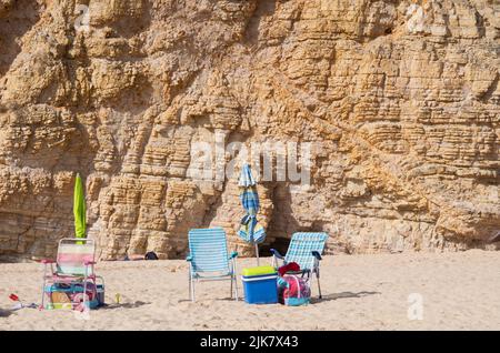 Sagres, Portogallo. 22nd luglio 2022. Sedie pieghevoli e ombrelloni chiusi si trovano di fronte ad un muro di roccia presso la spiaggia 'Praia do Beliche'. Credit: Viola Lopes/dpa/Alamy Live News Foto Stock