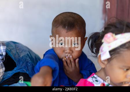 Un giovane thai guarda e tiene la mano in bocca mentre mangia Foto Stock