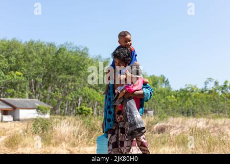 Un padre thailandese che vive tra gli alberi di gomma porta l'acqua dal pozzo mentre porta i suoi figli piccoli Foto Stock