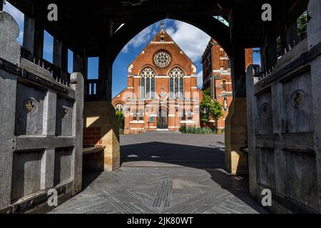 L'ingresso ovest di una chiesa vittoriana inglese in mattoni rossi, vista attraverso le porte in legno di Lych Foto Stock