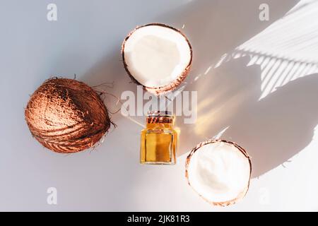 Olio di cocco e noci di cocco fresche su sfondo bianco all'ombra delle foglie di palma. Concetto di terapia alternativa. Vista dall'alto, piatto Foto Stock