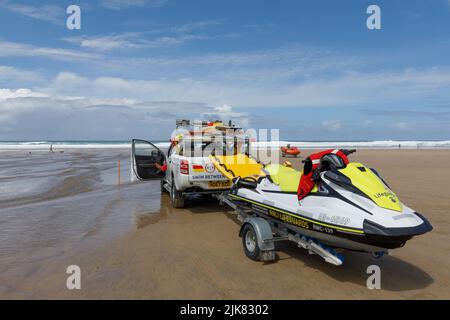 Bagnini sulla spiaggia. Un camion di raccolta della pattuglia RNLI si siede sulla spiaggia con un corridore d'onda su un rimorchio dietro Foto Stock