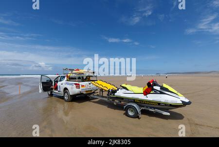 Bagnini sulla spiaggia. Un camion di raccolta della pattuglia RNLI si siede sulla spiaggia con un corridore d'onda su un rimorchio dietro Foto Stock