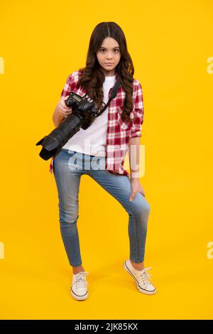 Tutta la lunghezza di ragazza teen con fotocamera professionale dslr con grande obiettivo fotografico. Fotografo di capretto isoalted su sfondo giallo. Scuola di fotografia. Foto Stock