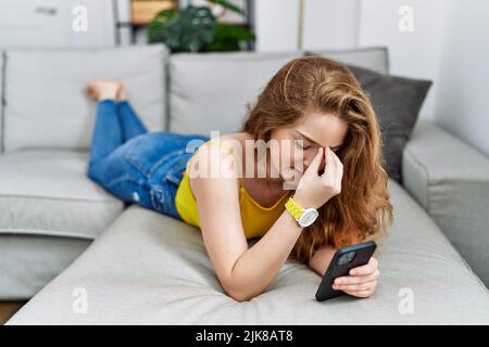 Giovane donna caucasica sdraiata sul divano con smartphone strofinando naso e occhi stanchi sensazione di affaticamento e mal di testa. Stress e frustrazione concetto. Foto Stock