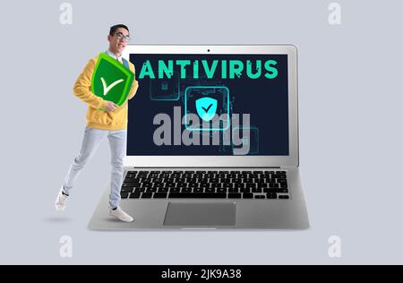 Giovane uomo asiatico con icona di antivirus e grande portatile su sfondo chiaro Foto Stock