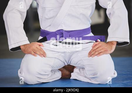 Rispetto dello sport. Un giovane irriconoscibile inginocchiato in pieno jiu jitsu gi in palestra. Foto Stock