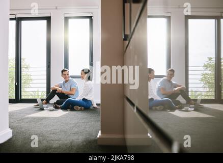 Weve ha ottenuto il nostro lavoro tagliato fuori per noi. Scatto a tutta lunghezza di una giovane coppia seduta sul pavimento insieme nella nuova casa e utilizzando un computer portatile. Foto Stock