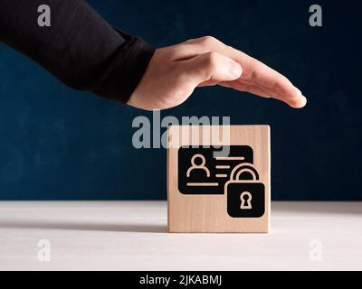 Protezione dei dati personali contro la criminalità informatica e il concetto di sicurezza informatica. La mano maschio protectively si erge sul blocco di legno con identità personale da Foto Stock