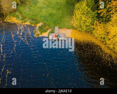 coppia posata sul molo al lago coperto di foglie autunnali Foto Stock