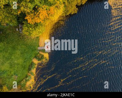 coppia posata sul molo al lago coperto di foglie autunnali Foto Stock