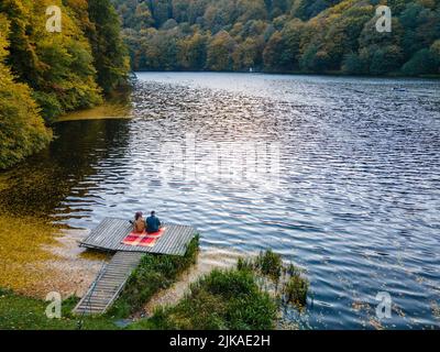 coppia posata sul molo al lago coperto di foglie autunnali Foto Stock