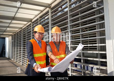 Team di ingegneri asiatici che discutono prima di Blueprint Foto Stock