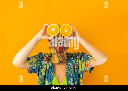 Donna irriconoscibile in maschera di dinosauro che tiene come i suoi occhi fresche fette di arancio. Cibo sano surreale. Foto Stock