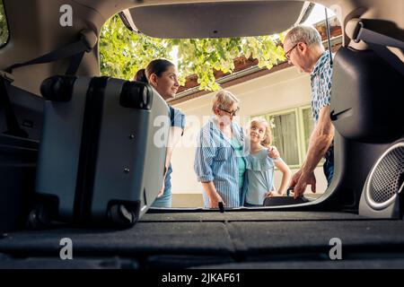 Persone che caricano trolley e borse in tronco, preparandosi a viaggiare in vacanza estiva viaggio stradale. Bambino piccolo e famiglia in partenza in vacanza viaggio con veicolo, andando in avventura con i nonni. Foto Stock