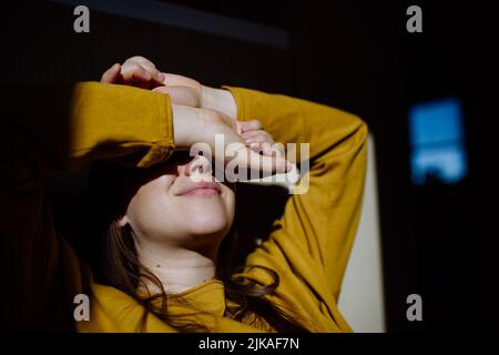 Donna che soffre di depressione e sdraiata sul pavimento con le mani che ricoprono la testa su sfondo nero. Foto Stock