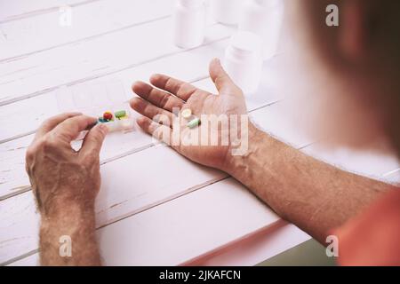 Mani di un uomo anziano che estrano le pillole dal contenitore Foto Stock