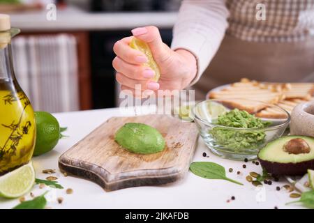 Fare toast avocado - Donna spremendo il succo di lime fresco su avocado mature dimezzate Foto Stock