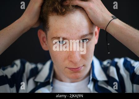 Ritratto di bel giovane uomo pensieroso con capelli zenzero e frane guardando via su sfondo nero, primo piano Foto Stock