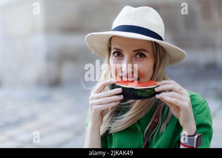 Giovane donna viaggiatore che mangia cocomero in strada durante caldo giorno di sole, concetto di vacanza estiva. Foto Stock