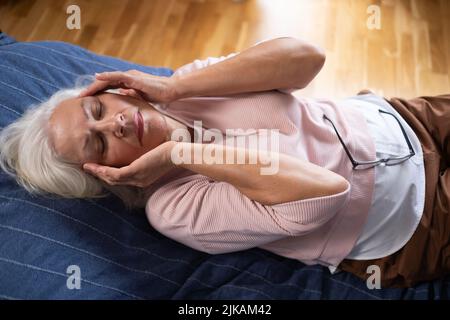 Donna anziana che ha mal di testa e tocca la testa con le mani a casa. Foto Stock