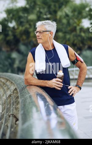 Uomo anziano che beve acqua dopo aver fatto jogging al mattino Foto Stock