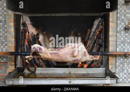 La carcassa di una pecora giovane arrostisce su uno spiit sopra un fuoco basso in forno. Agnello arrosto su uno spiedo. Cucina all'aperto. Cucina locale a Dagestan. R Foto Stock