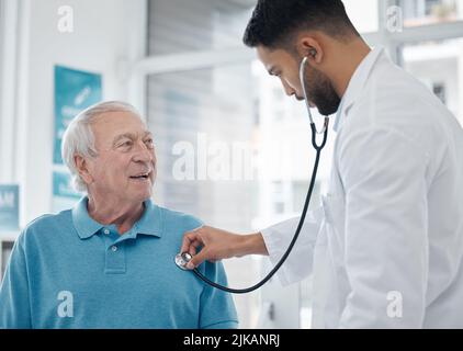 Respira dentro e fuori per me. Un medico giovane che esamina un uomo maturo con uno stetoscopio in un ufficio. Foto Stock