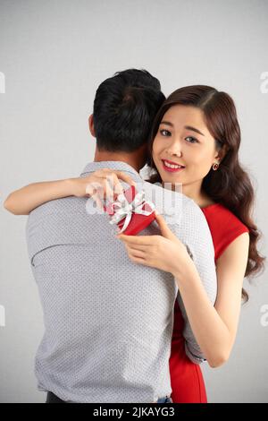 Bella giovane donna abbracciando il suo uomo e tenendo in mano una piccola scatola regalo rossa Foto Stock