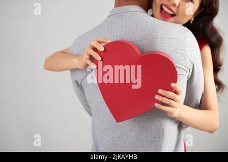 Donna felice che tiene la scatola del regalo a forma di cuore mentre abbraccia il suo marito Foto Stock