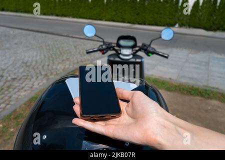 La mano di una donna che utilizza un telefono cellulare scansiona il codice QR su uno scooter motociclistico in una giornata di sole. Concetto di noleggio di trasporto Foto Stock